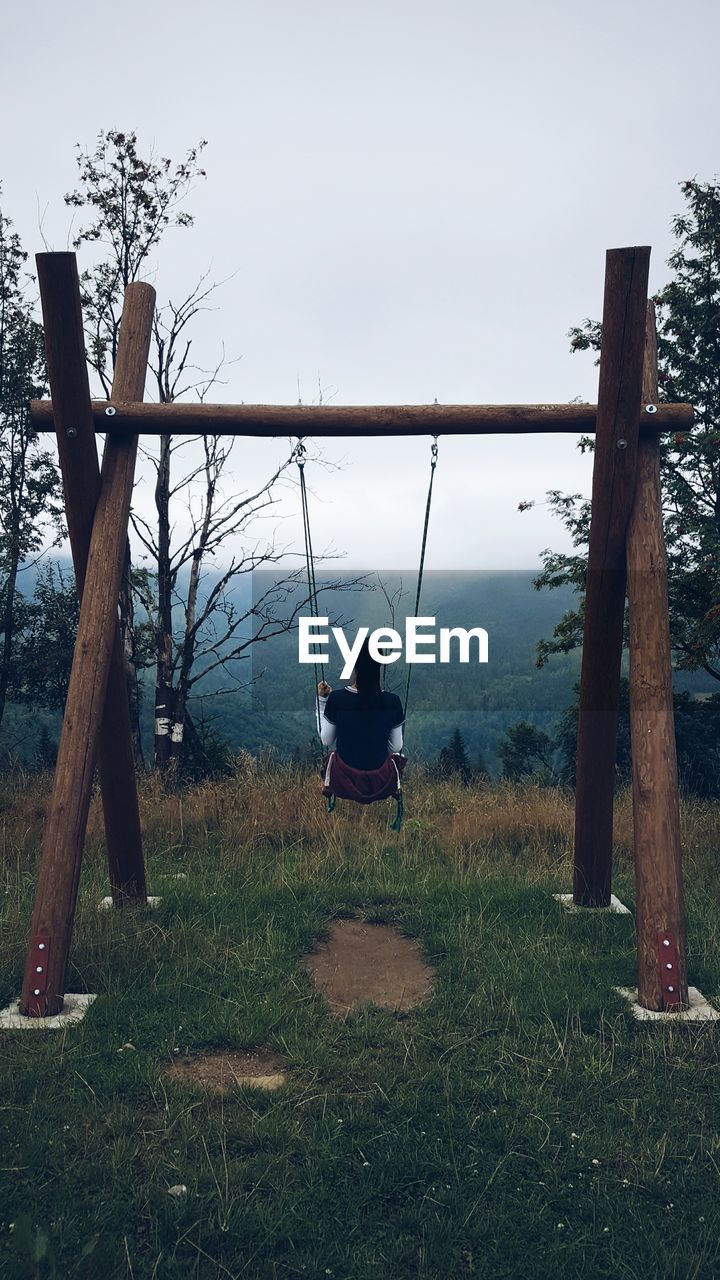 Rear view of young woman sitting on swing during foggy weather