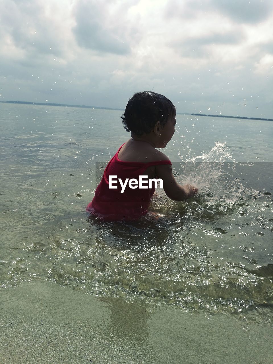 Rear view of baby girl playing on beach against sky