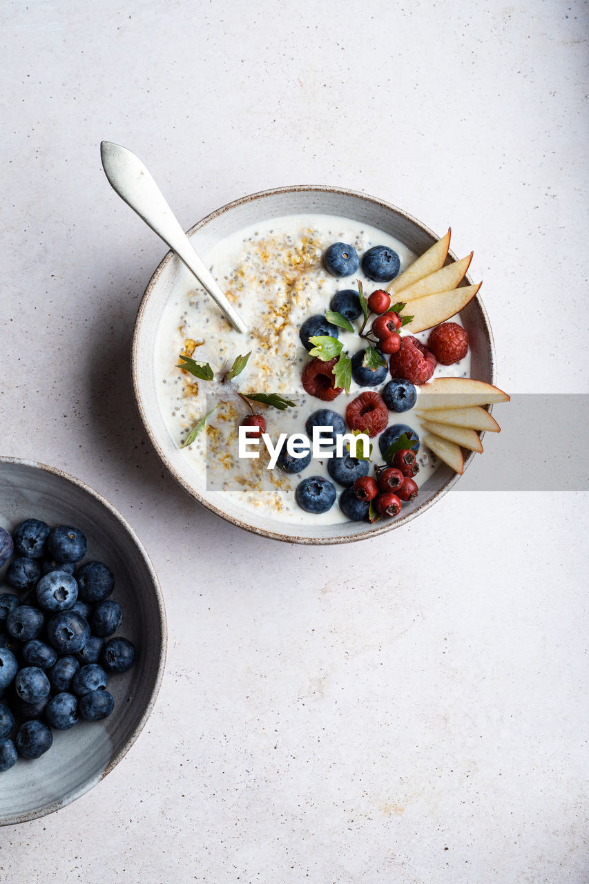 Top view bowl of delicious porridge topped with blueberries and raspberries near slices of pear served on table during breakfast