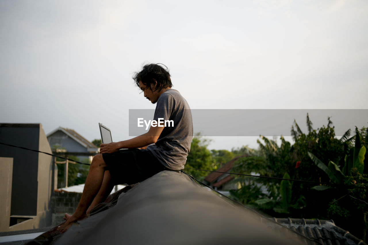 Side view of young man sitting and working at rooftop