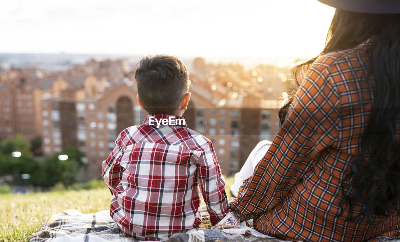 Mother and son looking at view while sitting on hill during sunset