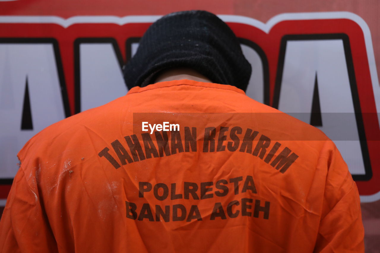 REAR VIEW OF PERSON WITH TEXT AGAINST ORANGE WALL
