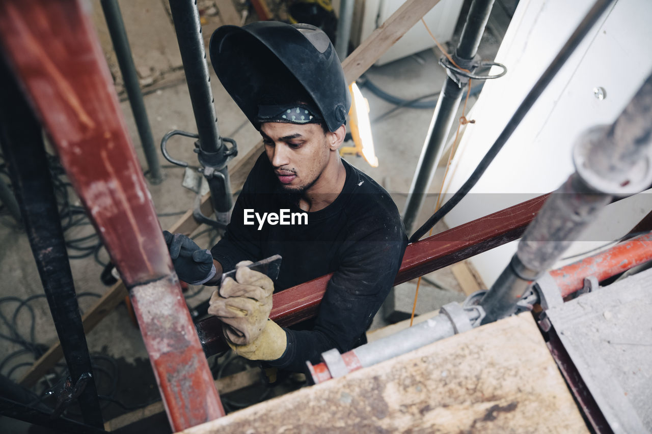 Young male welder wearing welding helmet while working at construction site