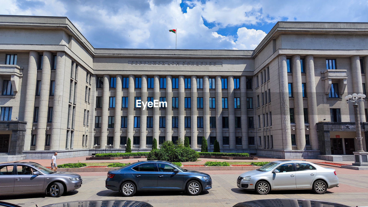 architecture, car, motor vehicle, mode of transportation, transportation, building exterior, built structure, city, building, vehicle, government, street, downtown, sky, travel, travel destinations, land vehicle, neighbourhood, nature, facade, cloud, day, plaza, flag, road, outdoors, history, residential area, the past, no people