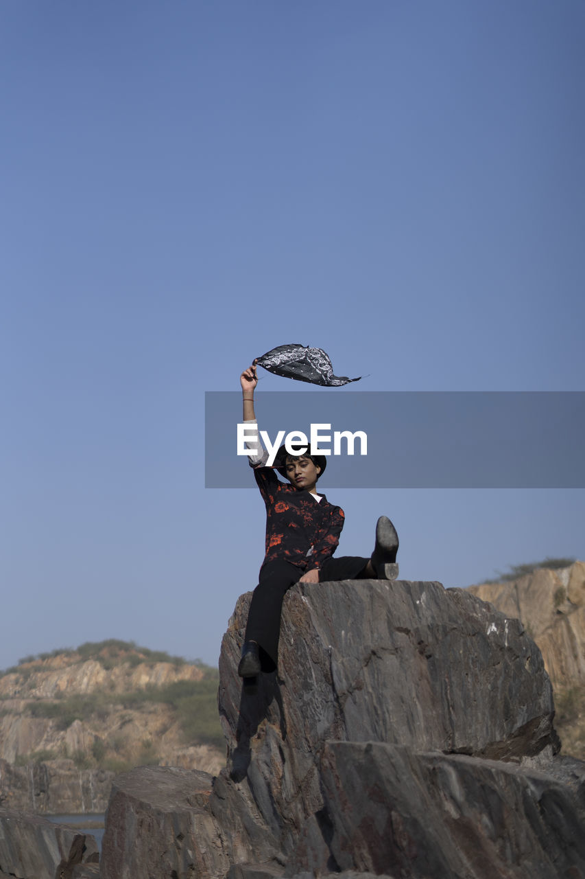 WOMAN STANDING ON ROCK AGAINST SKY