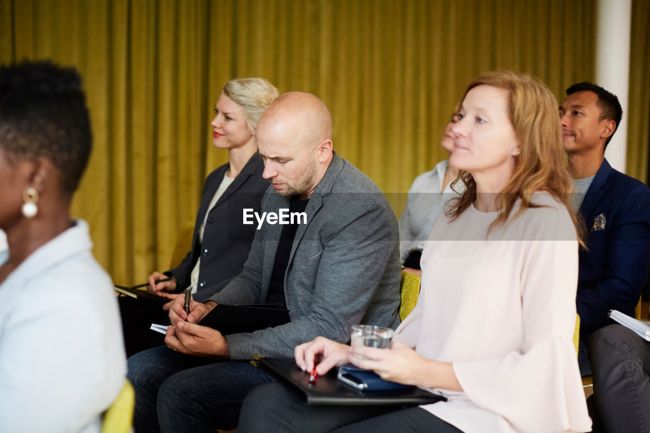 Male entrepreneur writing while sitting with colleagues in seminar at workplace