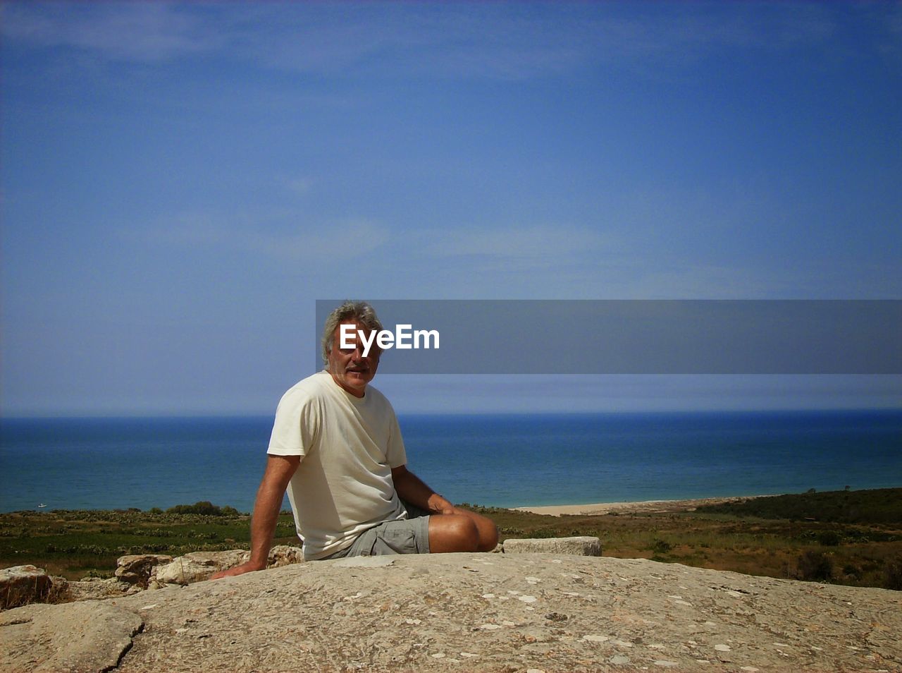 Portrait of man sitting on rock against sea and sky