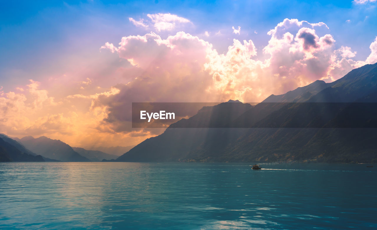 Scenic view of lake and mountains against cloudy sky during sunset