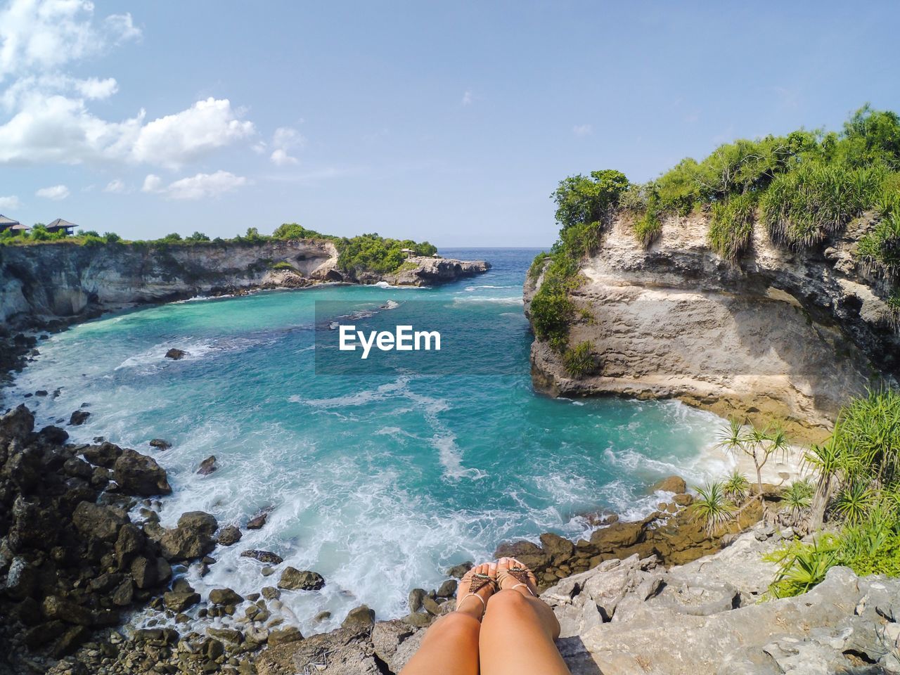 Low section of woman sitting on cliff in front of sea