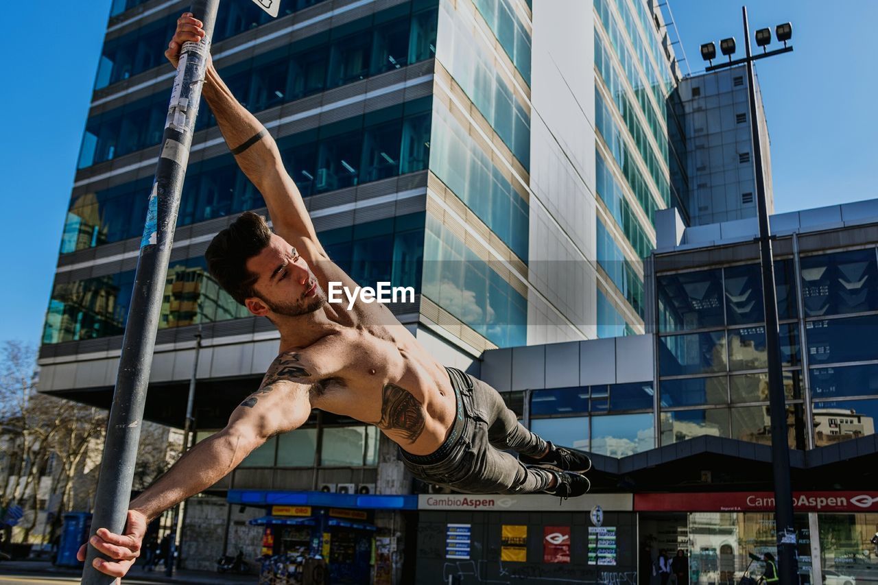 Low angle view of shirtless young man exercising against building in city