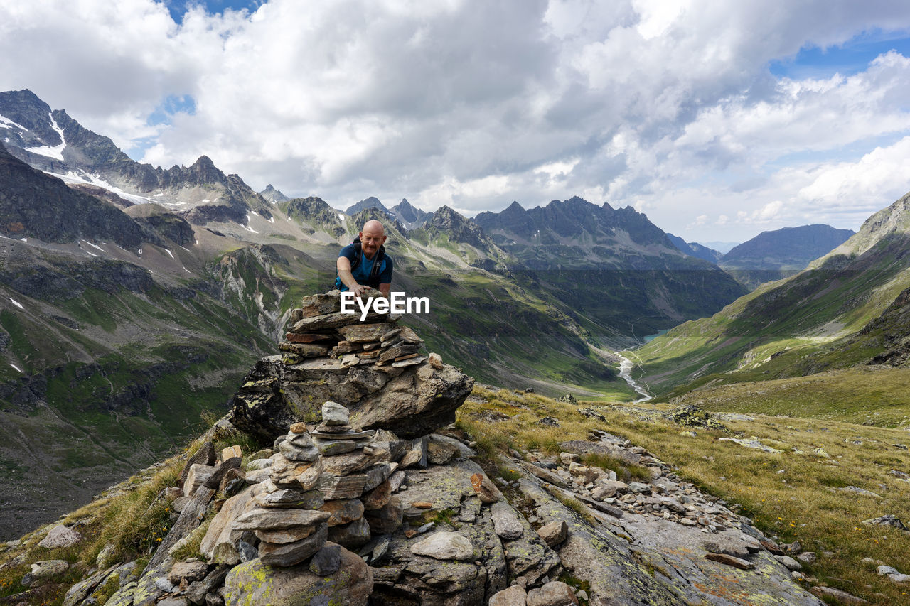 Bald man stacking rocks against mountains and cloudy sky