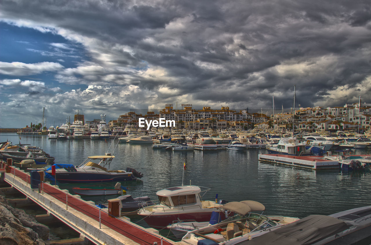 Boats moored at harbor in sea against cloudy sky