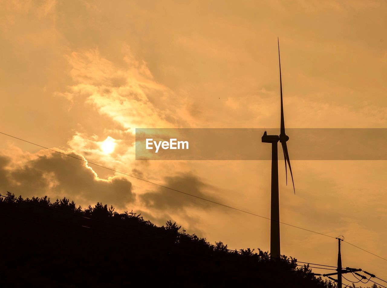 Low angle view of silhouette wind turbine and plants against cloudy sky during sunset