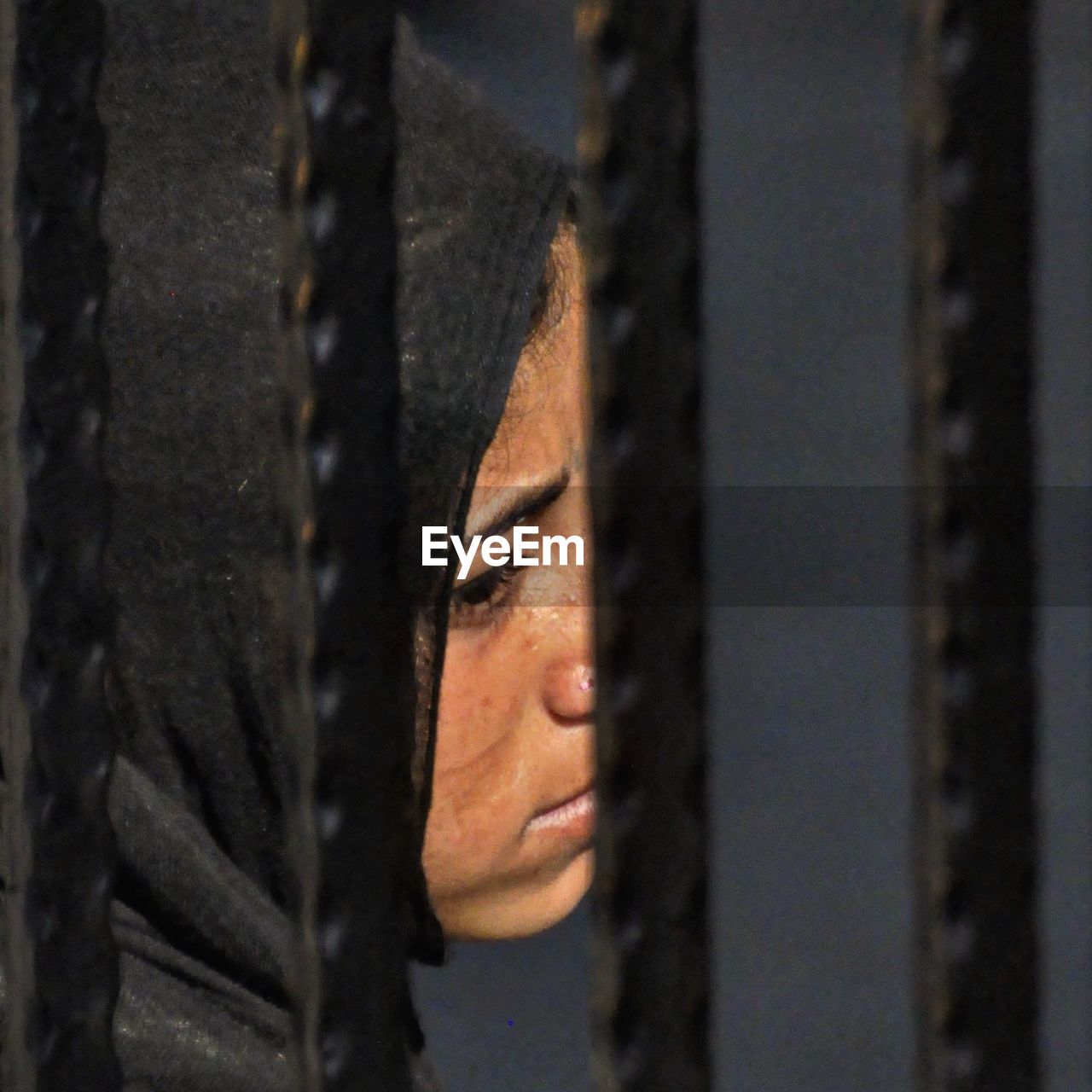 Close-up of sad woman in hijab seen through fence