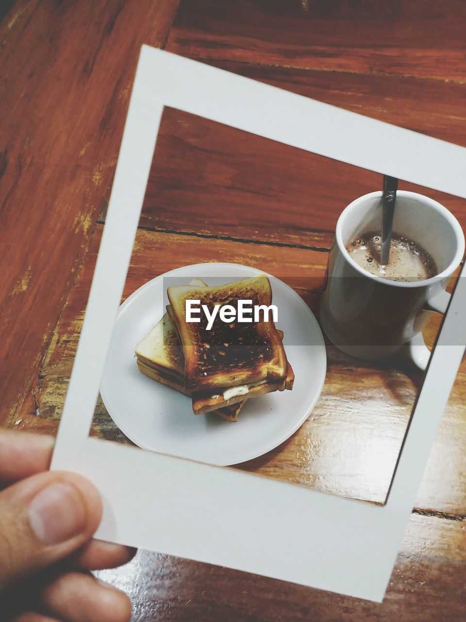 Cropped image of hand holding breakfast photograph against wooden table