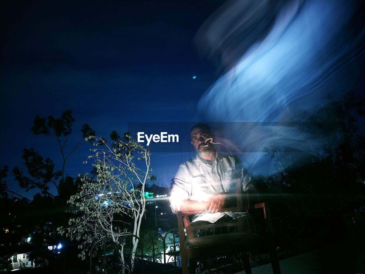 Digital composite image of man and illuminated lighting equipment against sky at night