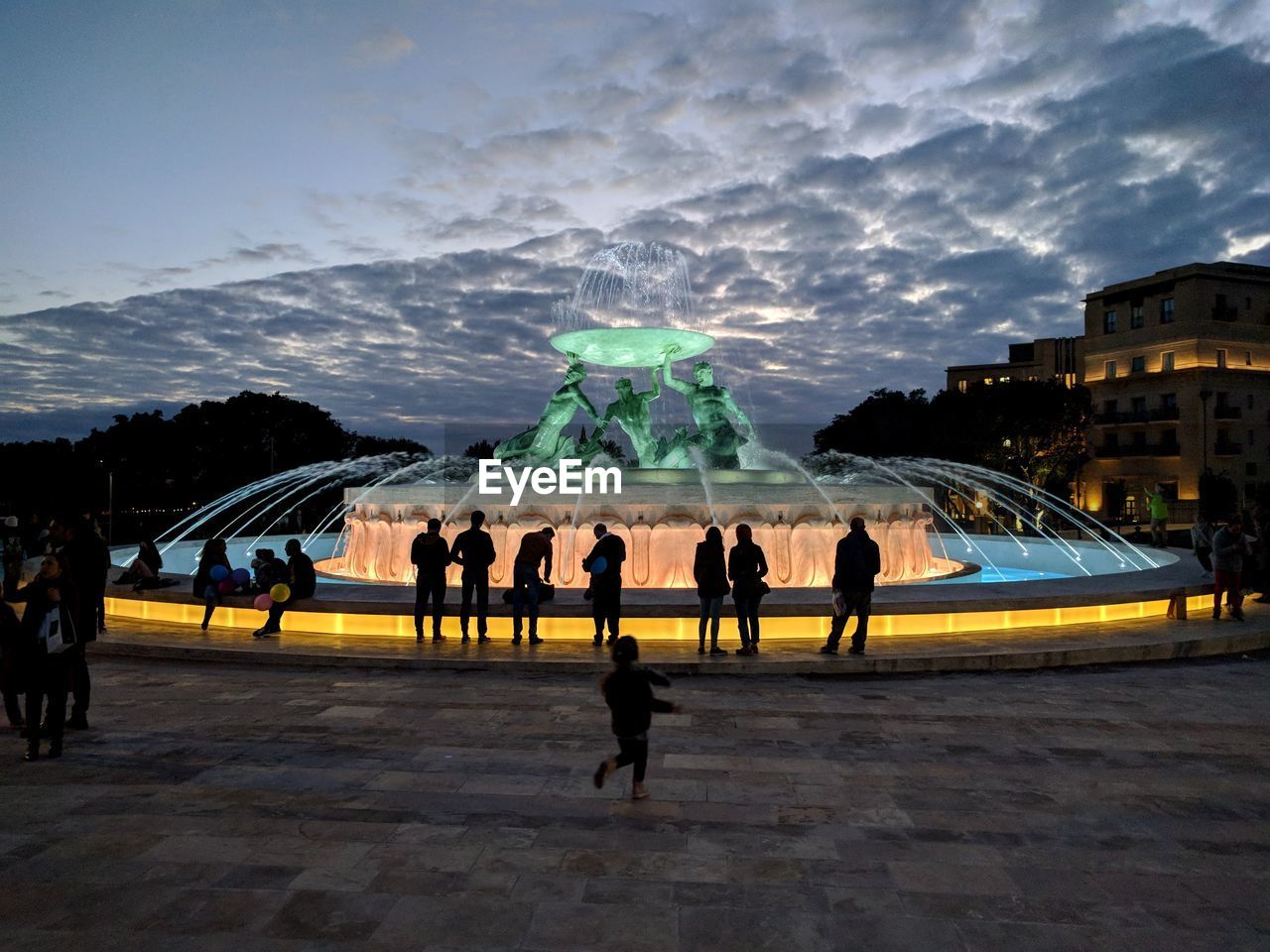 People at fountain in city against sky