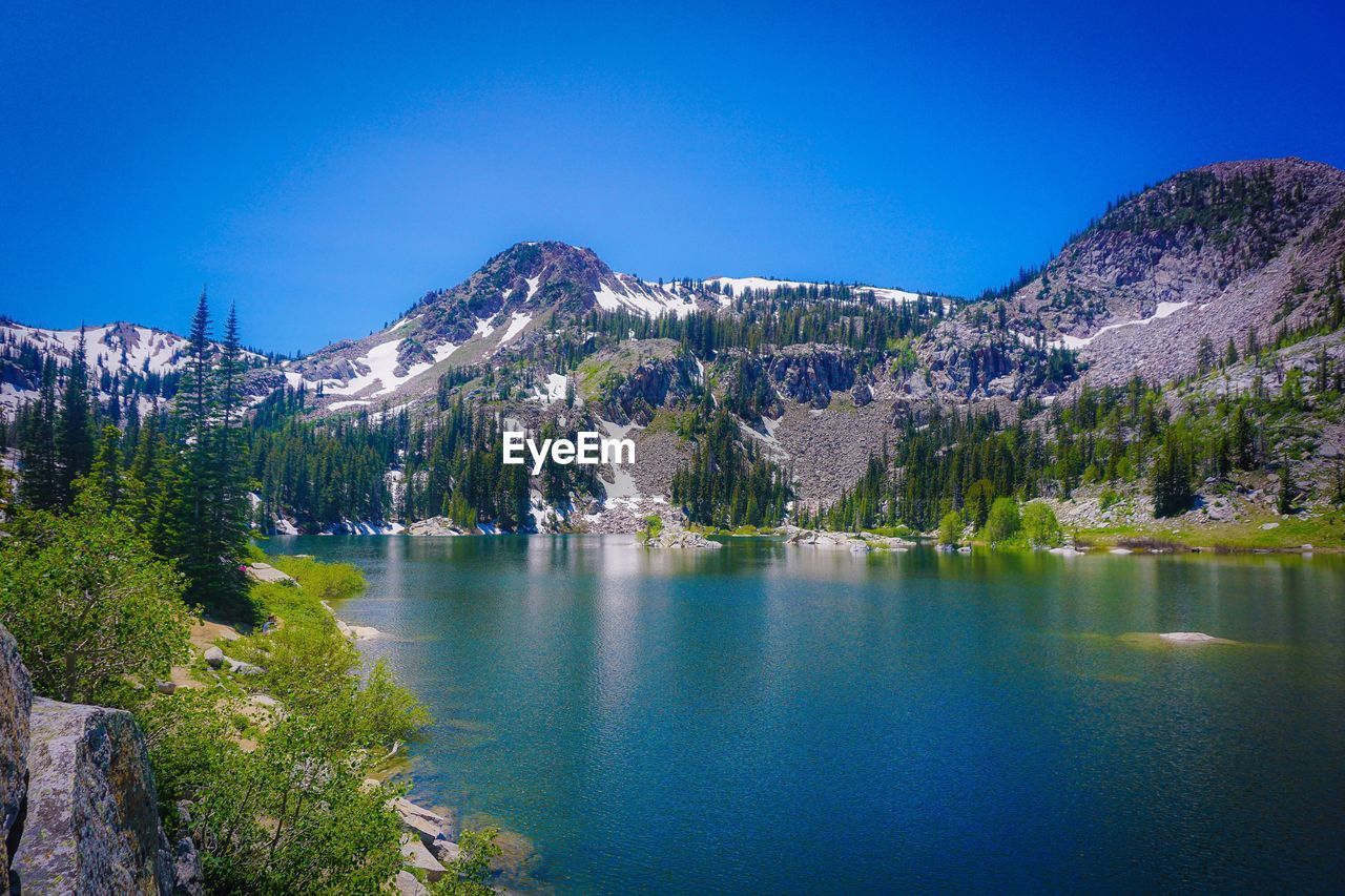 Scenic view of lake and mountains against clear blue sky