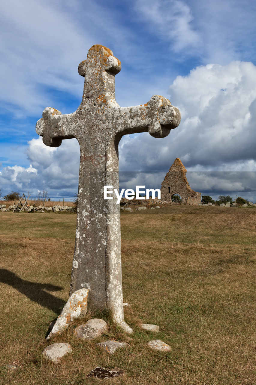 Cross on field against cloudy sky