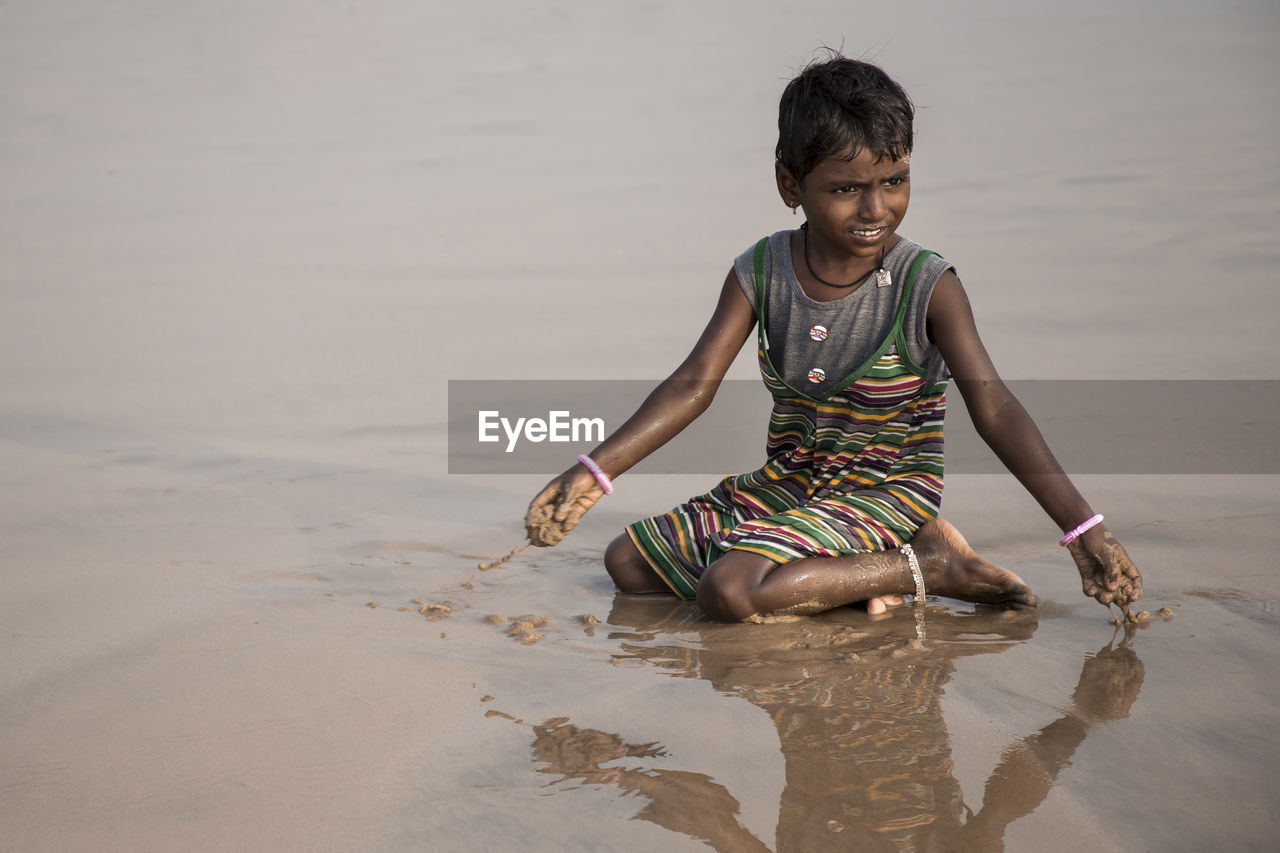 PORTRAIT OF HAPPY YOUNG WOMAN IN SAND AT BEACH