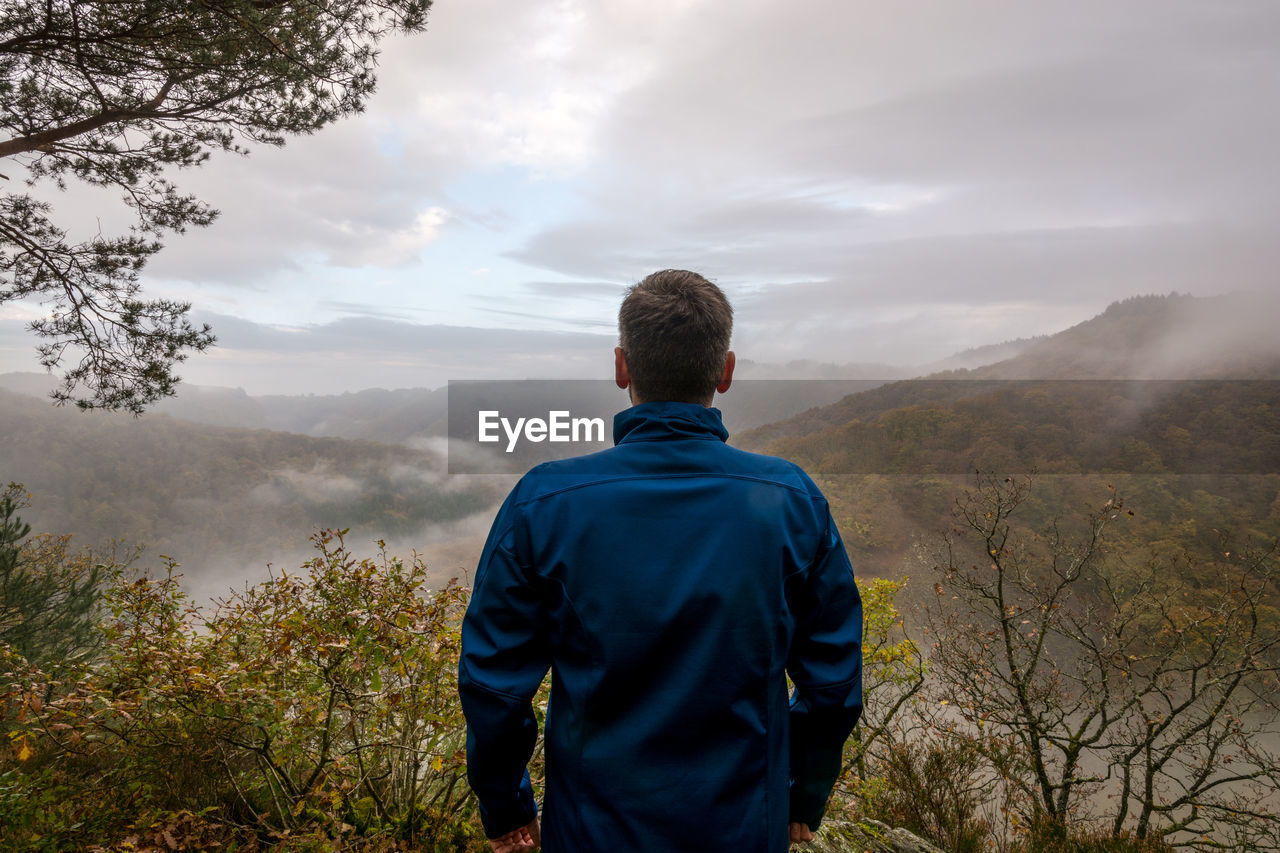 Rear view of hiker standing on mountain against sky during sunset