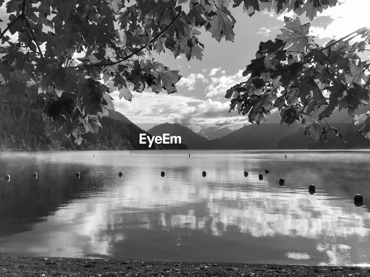 Black and white landscape of a lake, reflection of clouds and mountains in the background