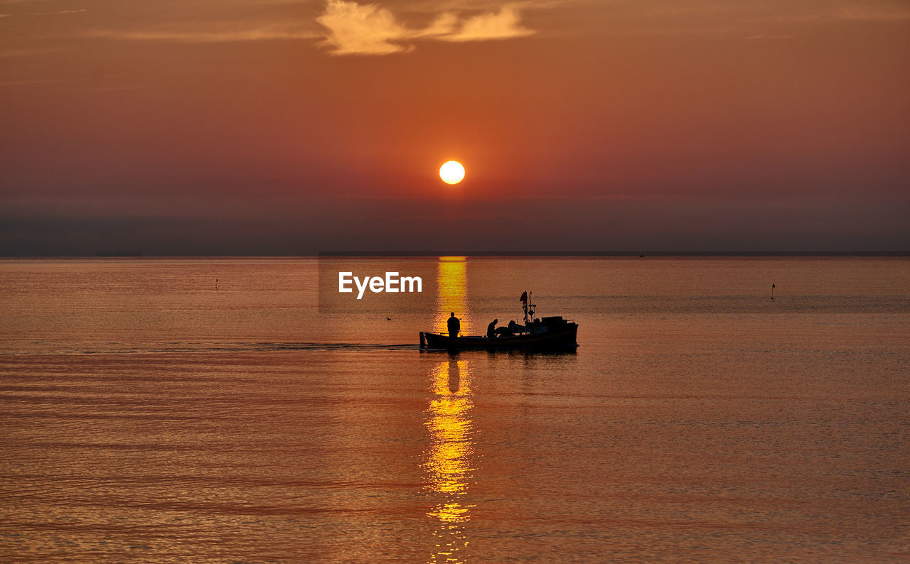 Silhouette men on boat in sea against sky during sunset