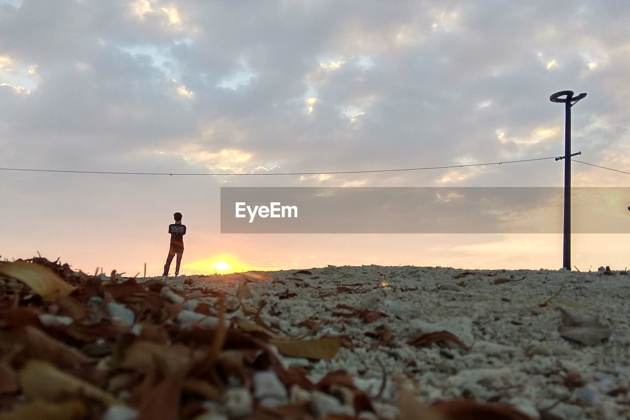 Rear view of man standing on sand against sky during sunset