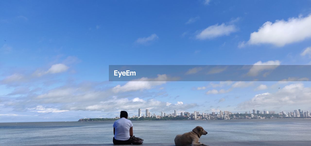 Rear view of woman with dog at sea against sky