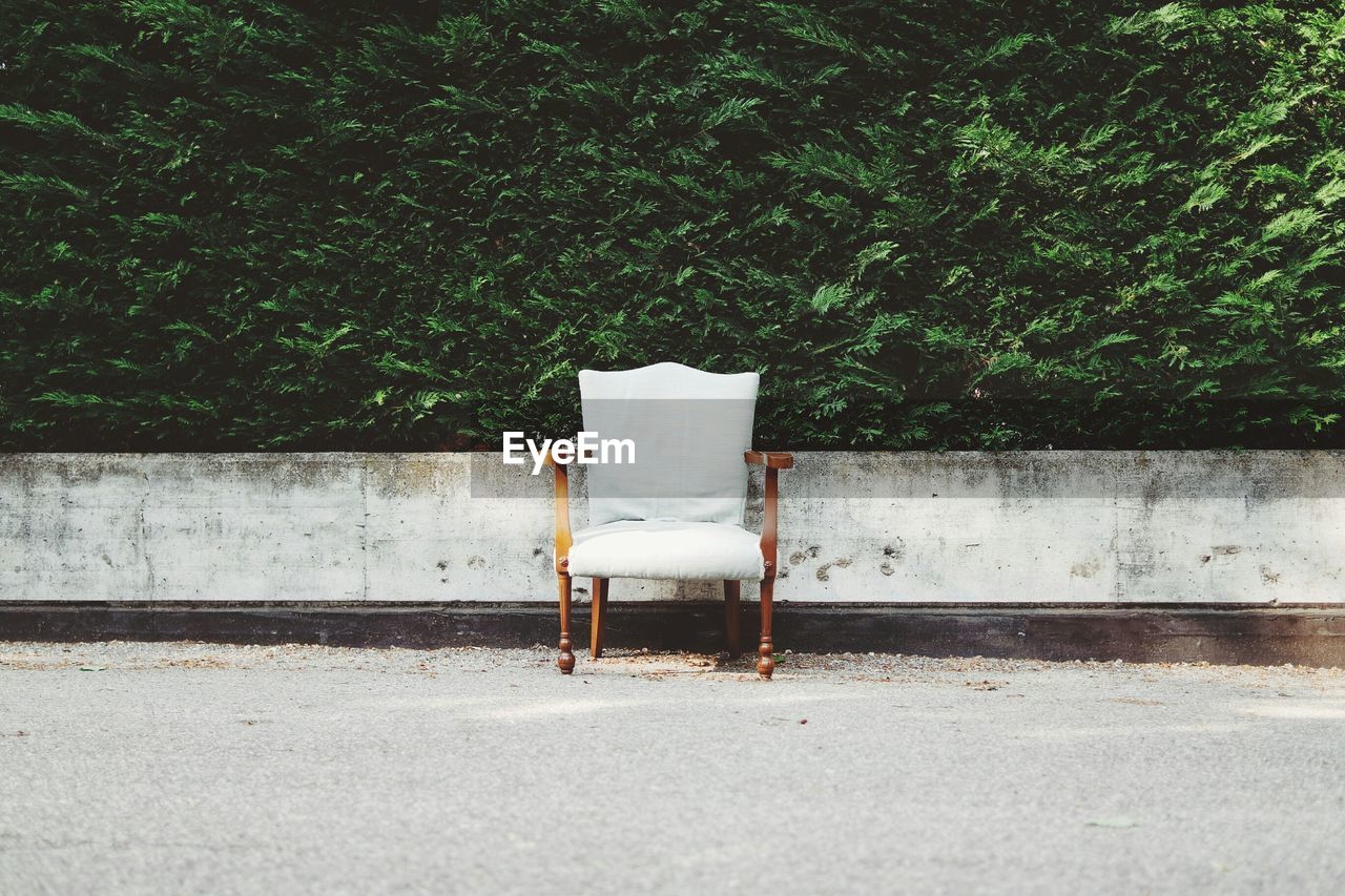 Wooden armchair on street in front of lush green leaves