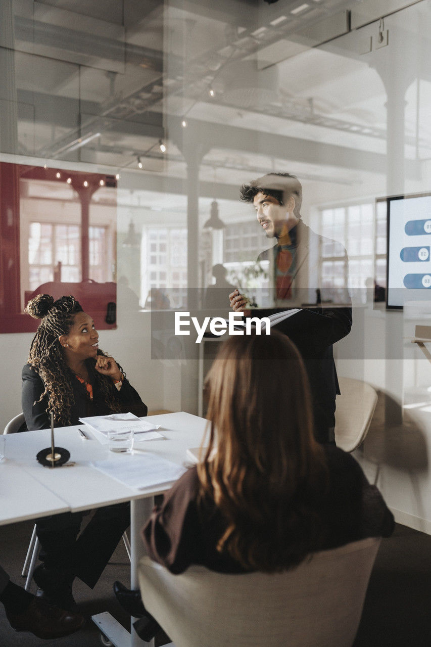 Businessman discussing with female colleagues in meeting at office seen through glass