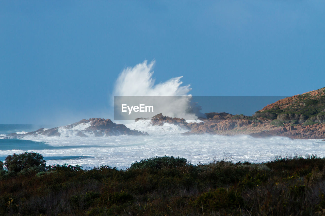 Water splashing at rock formation against blue sky