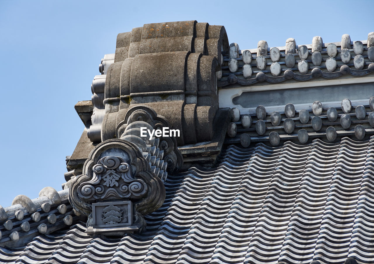 Low angle view of ornate tiles on building roof against sky
