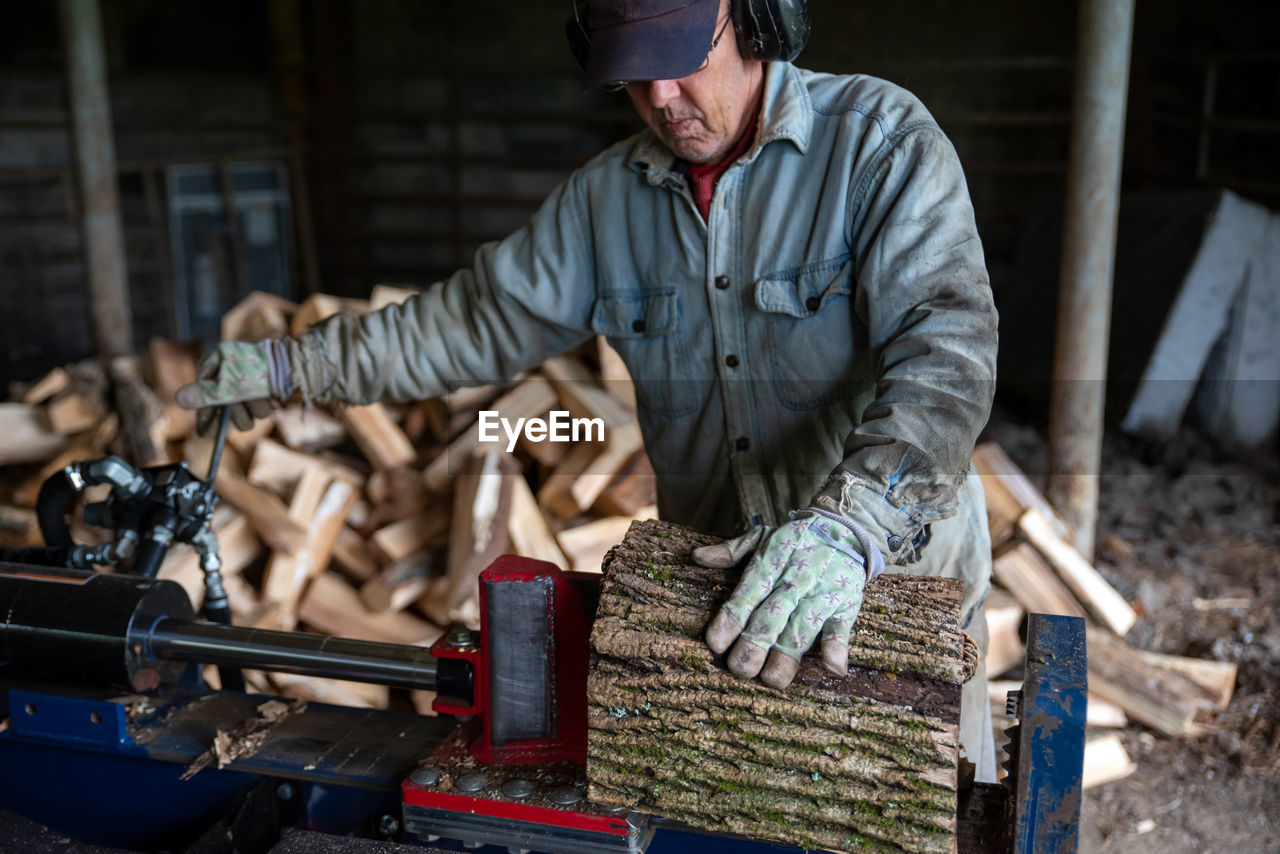 A man with work gloves and safety ear protectors uses hydraulic log splitter