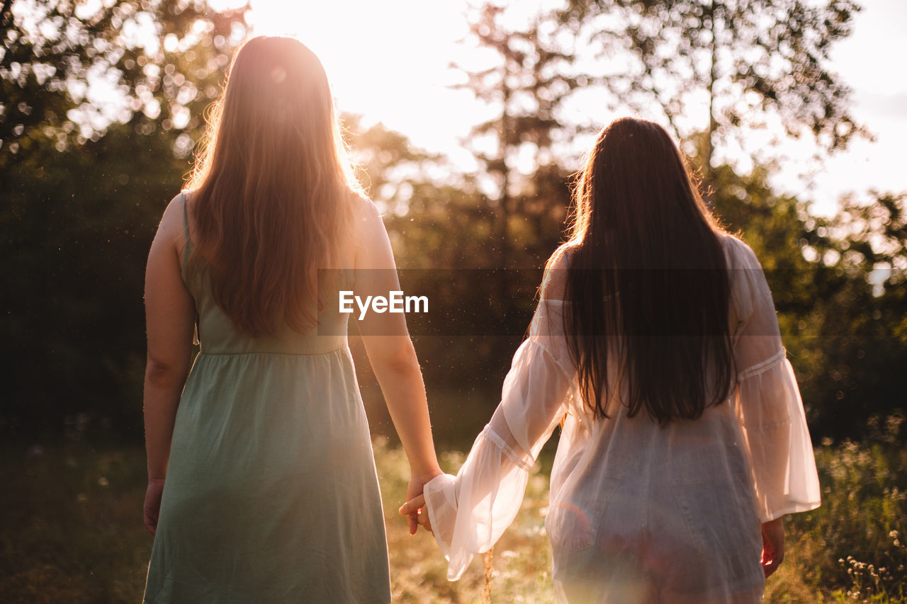 Back view of lesbian couple holding hands while standing in forest