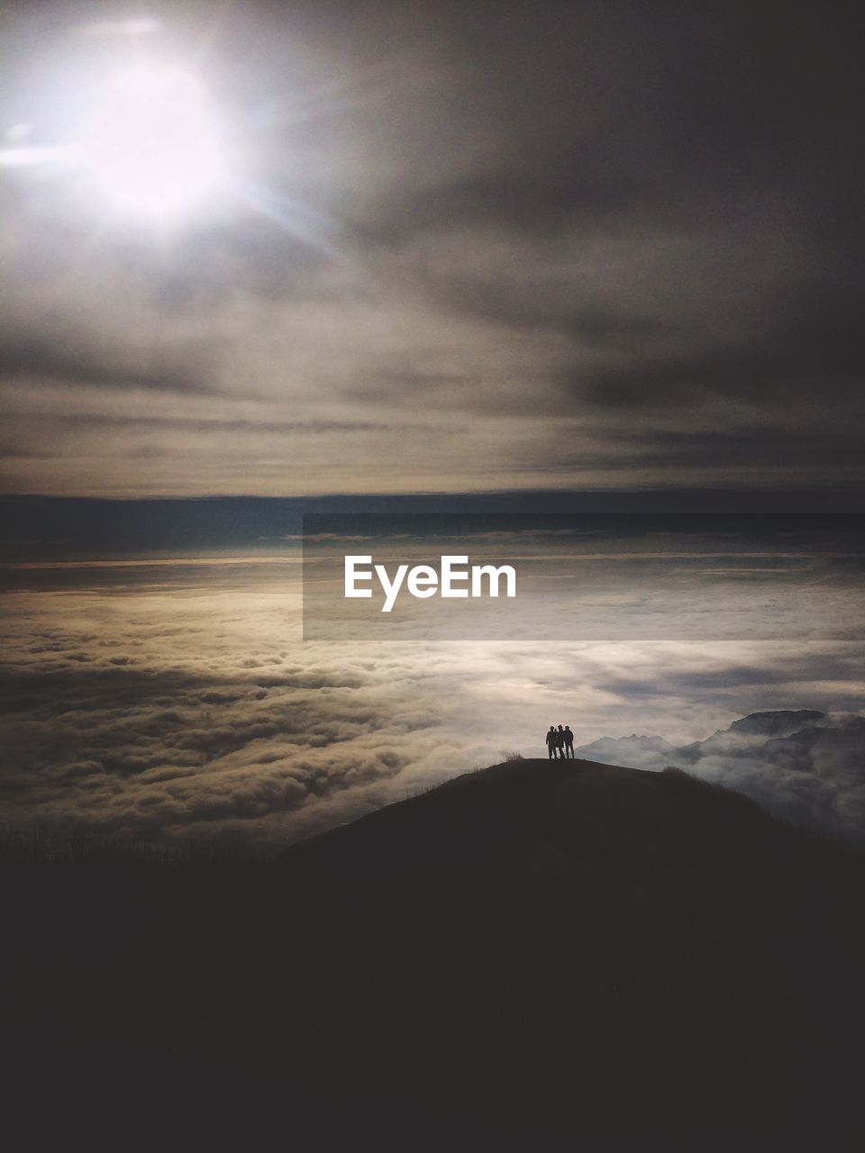 Aerial view of silhouette people standing on mountain against cloudy sky during sunny day