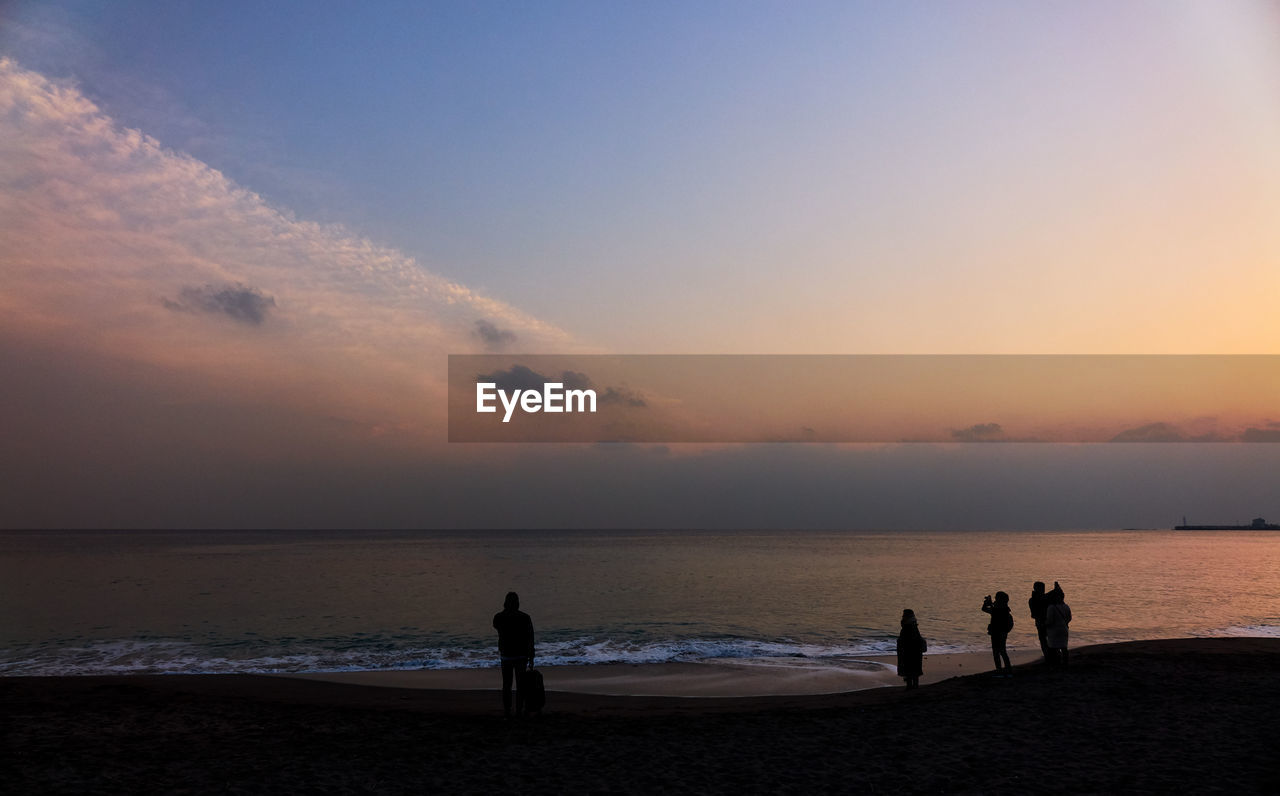 Silhouette people at beach against sky during sunset