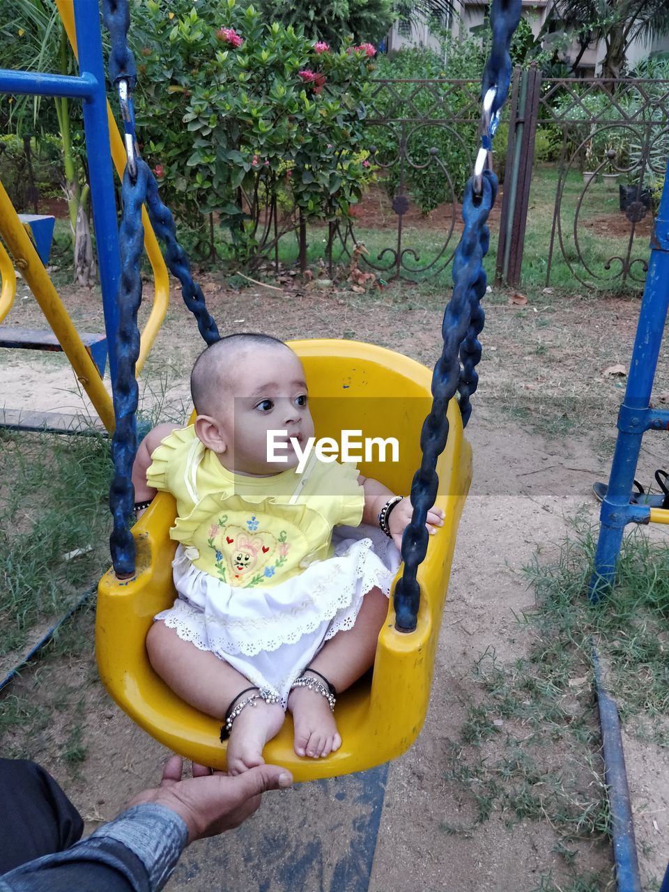 Midsection of man by girl sitting on swing