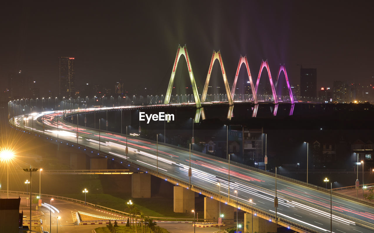 LIGHT TRAILS ON BRIDGE OVER RIVER IN CITY AT NIGHT