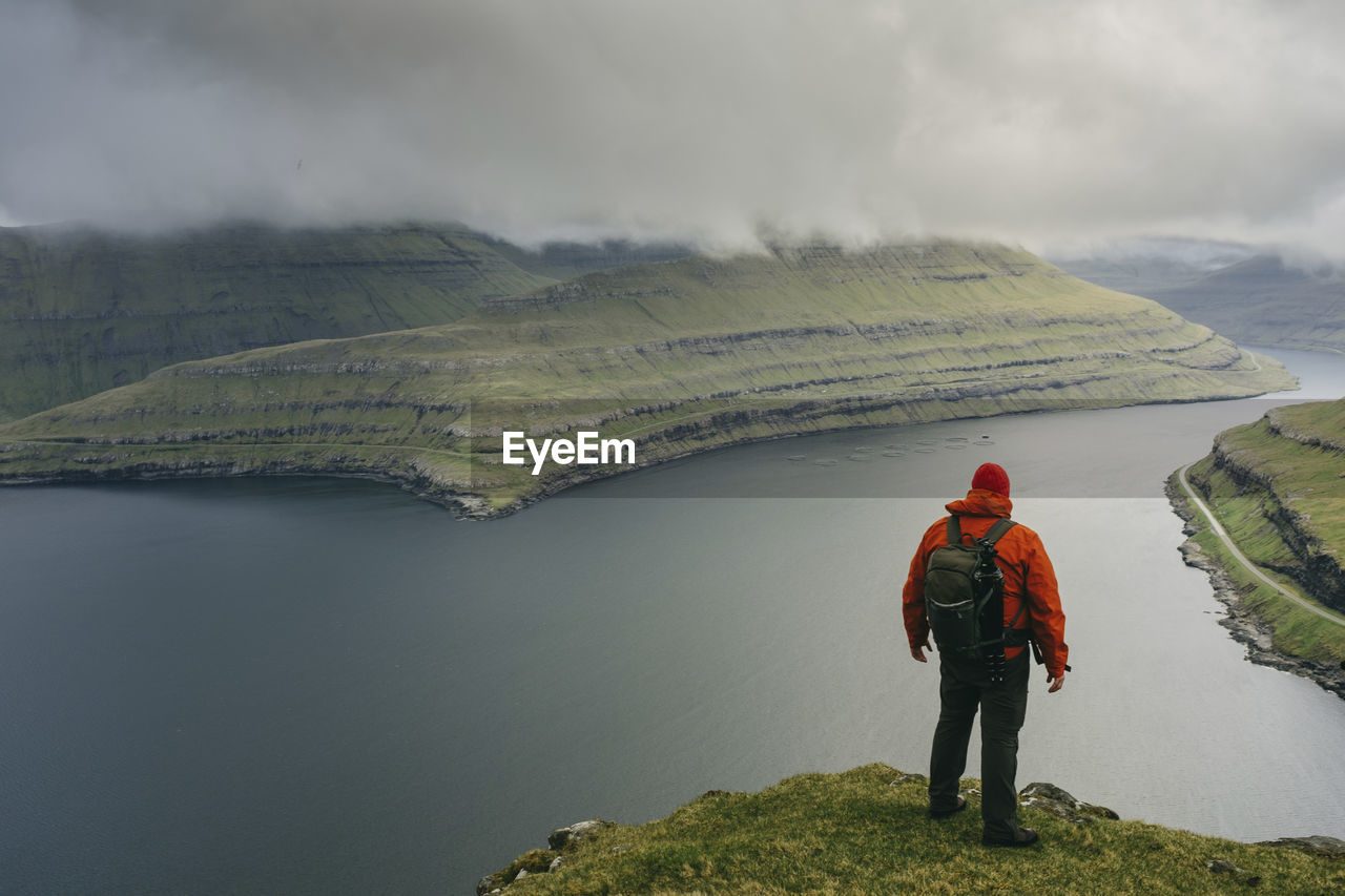 Hiker with backpack looking at view while standing on cliff against stormy clouds