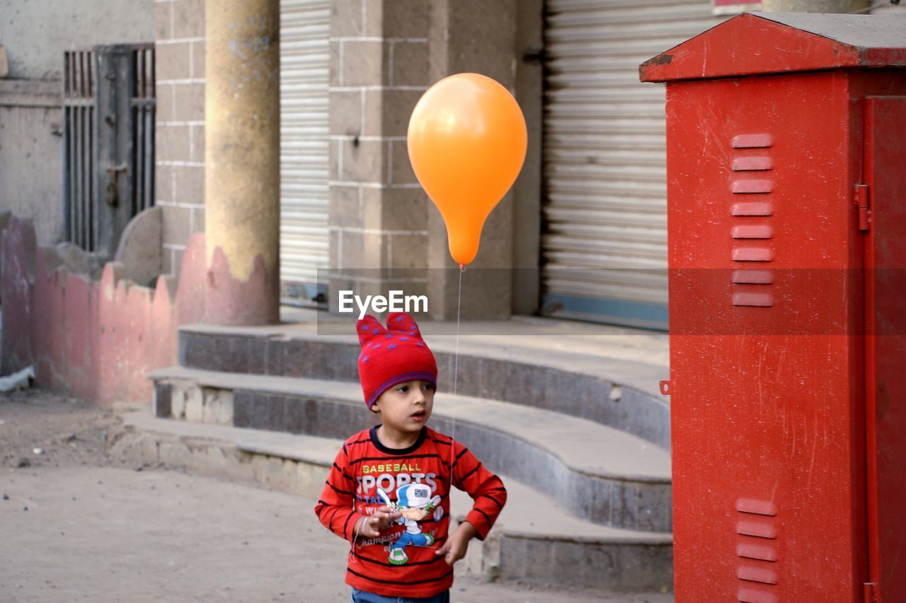 Cute boy holding balloon while standing against building