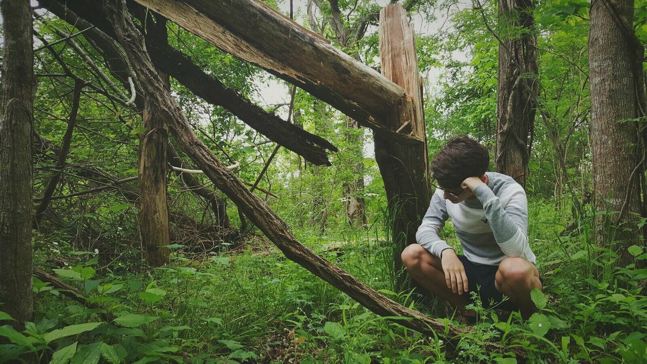 FULL LENGTH OF WOMAN SITTING ON TREE IN FOREST