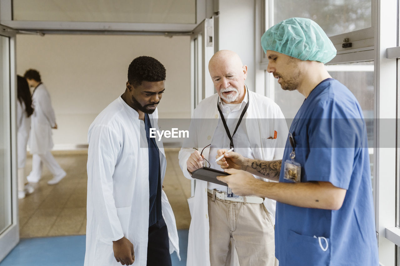 Physician and doctors discussing over digital tablet while standing in corridor at hospital