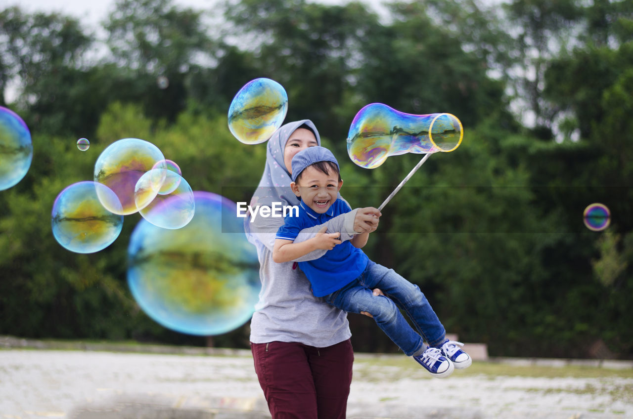 Mother and son making bubbles with wand against trees