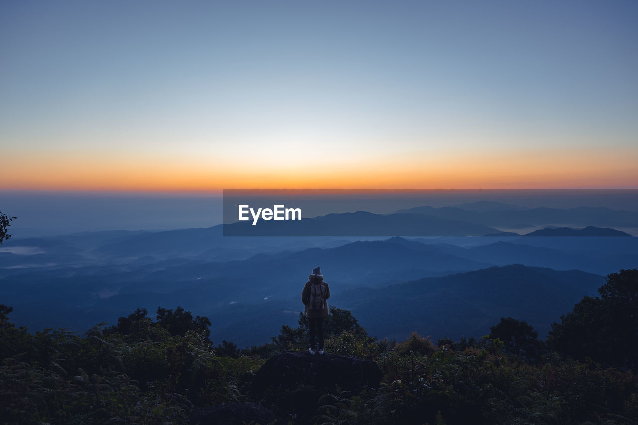 Rear view of silhouette man standing on mountain against sky at sunset