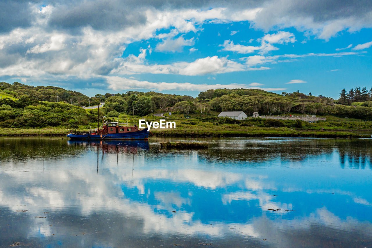 Scenic view of clifden bay at high tide against blue sky with a fishing boat anchored in the water