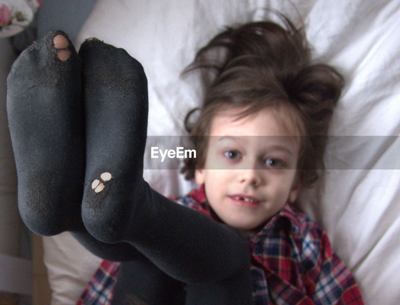 High angle portrait of boy wearing socks while lying on bed