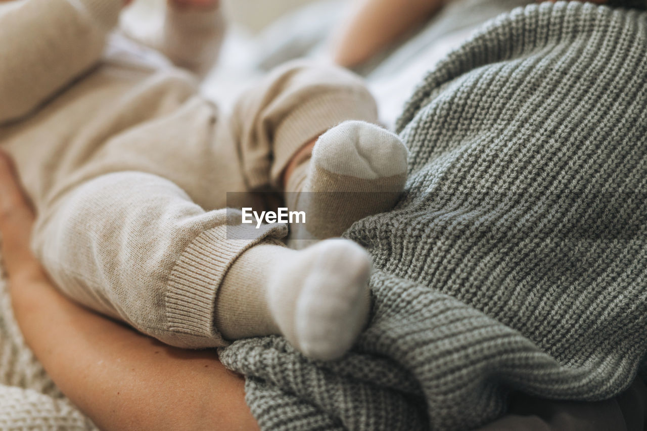 Cute baby feet in beige socks, child with mother on bed, happy motherhood