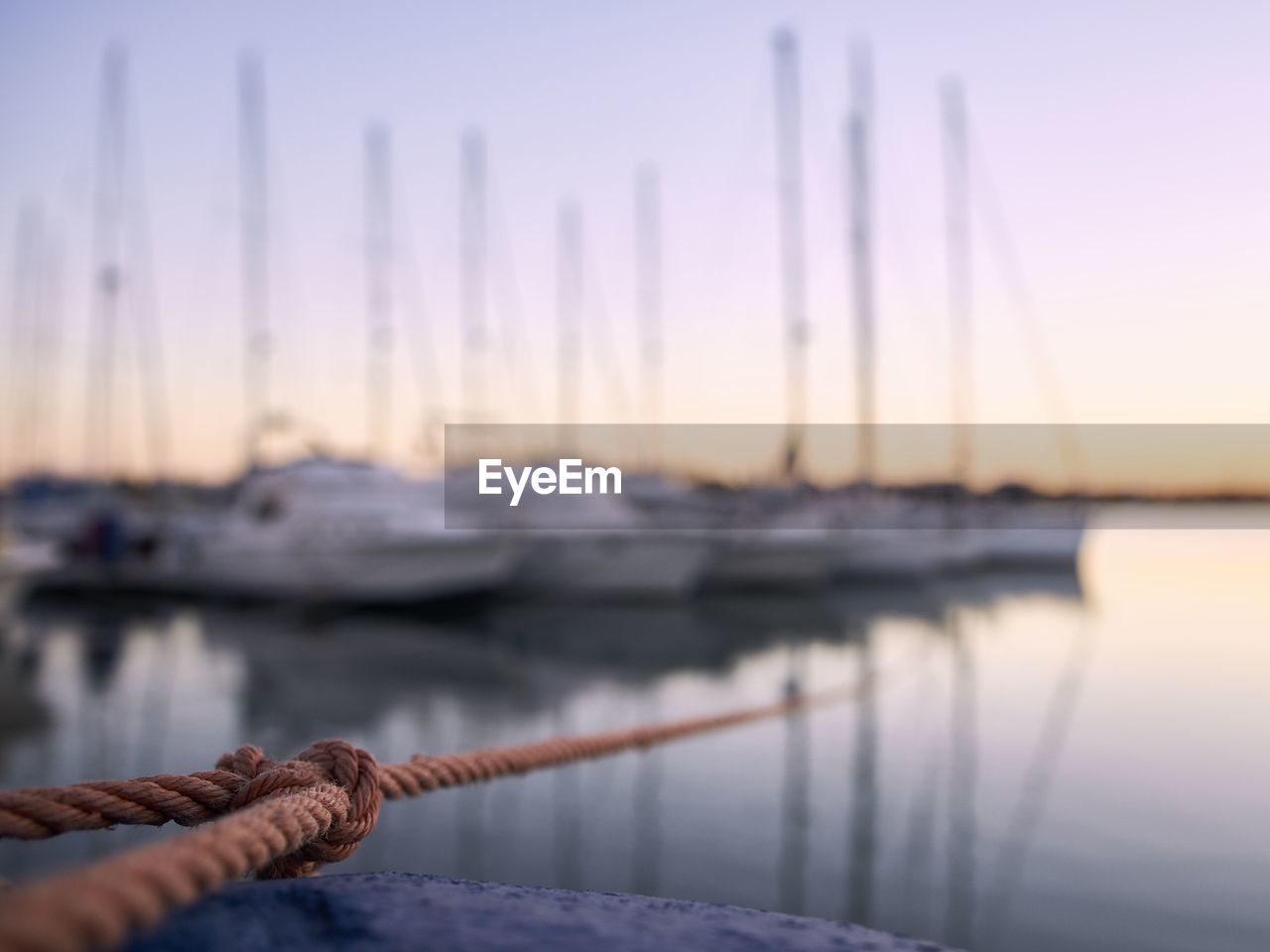 Close-up of rope against sailboats moored in sea at sunset