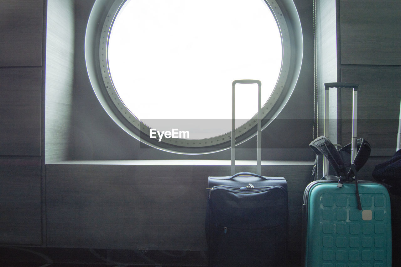 Two suitcases for traveling in front of the round porthole of the ship